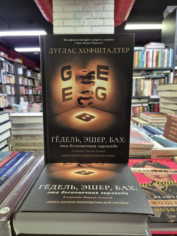 Обложка Дугласа Хофштадтера «Гедель, Эшер, Бах» крупным планом в книжной лавке: тёплое освещение и другие книги вокруг создают атмосферу чтения.
