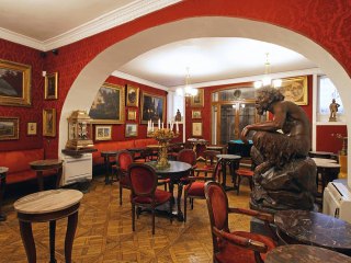 Красный зал с арочными проёмами и скульптурой в центре: исторический декор, деревянные полы и столики в классическом стиле кафе.