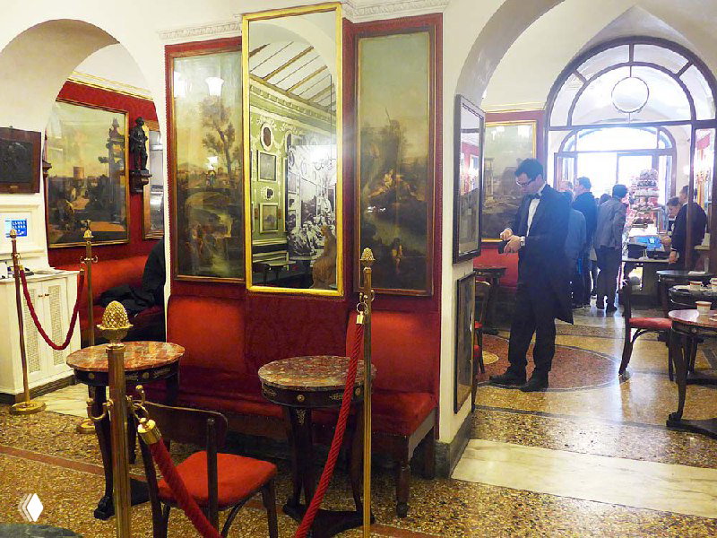 Вид на главный зал кафе с посетителями у входа: люди, очередь и яркое дневное освещение, создающее ощущение туристического наплыва.