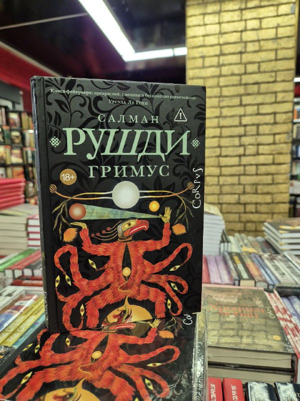 Переплет романа Салмана Рушди «Гримус» с ярким декоративным дизайном, стоящий вертикально на столе в книжном магазине.