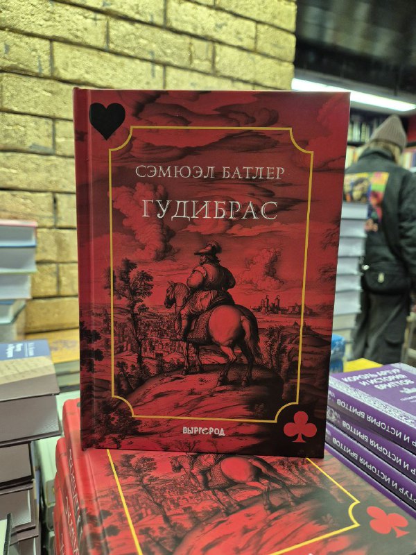 Красная обложка «Гудибраса» Батлера в декоративном исполнении, поставленная вертикально на стопке книг в магазине.