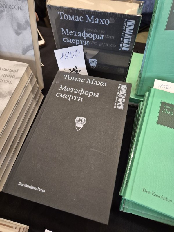 Книга Томаса Махо 'Метафоры смерти' с ценником 1800 на прилавке ярмарки Rassvet, крупный план обложки и рядом другие издания.