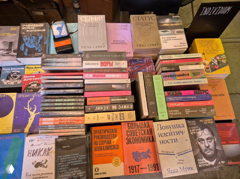 Общий план прилавка с множеством стопок книг разных издательств, разноцветные корешки и расставленные ряды — типичная сцена ярмарки Rassvet.