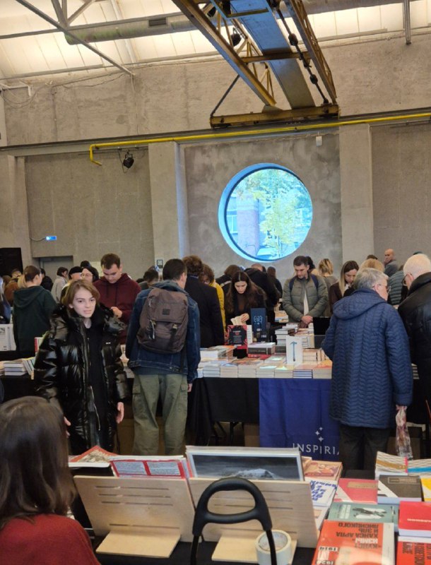 Зал ярмарки Rassvet: посетители у прилавков, люди рассматривают книги и общаются с продавцами, кадр передает атмосферу мероприятия.