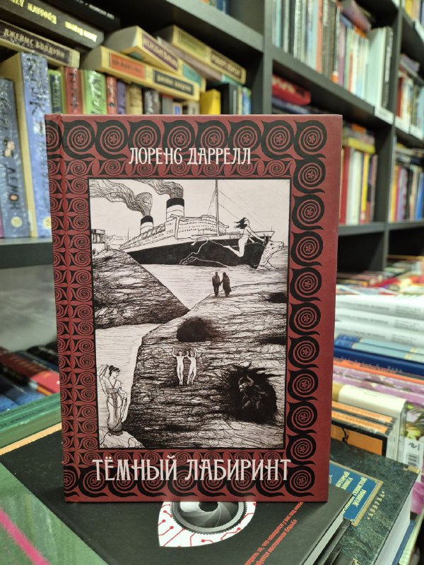 Фотография издания Лоуренса Даррелла «Темный лабиринт» в оформлении с чёрно‑белой гравюрой на фоне полок книжного магазина.