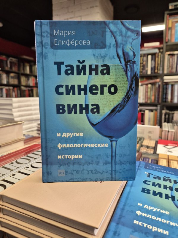 Книга Марии Елифёровой «Тайна синего вина» в голубой обложке, выставленная на столе; вокруг другие экземпляры и фон магазина.