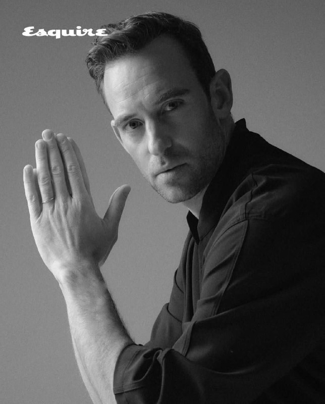 Ч/б портрет Жоэля Диккера в три четверти: руки сложены, акцент на мимике и текстуре одежды, стилизация под классическую мужскую съемку.