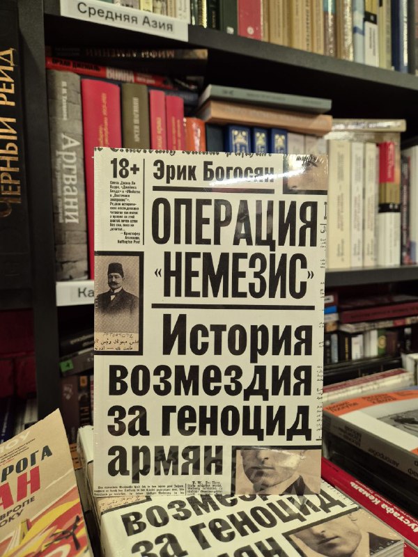Обложка книги «Операция "Немезис"» Эрика Богосяна крупным планом на прилавке книжного магазина с полками на фоне