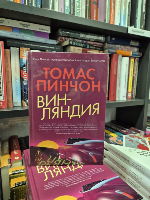 Яркая обложка переиздания «Винляндия» Томаса Пинчона на витрине книжного магазина, книги вокруг на заднем плане