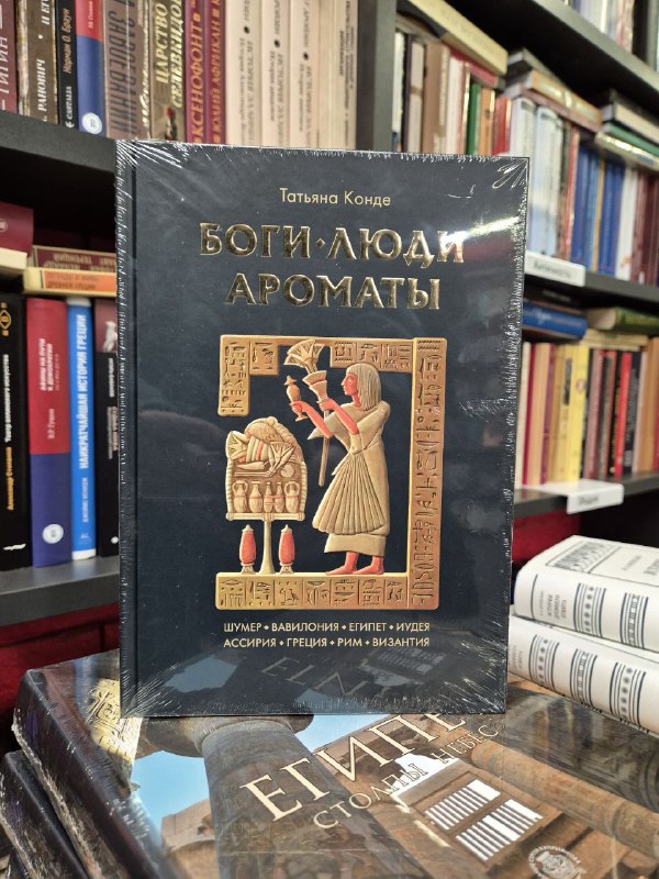 Обложка «Боги, люди, ароматы» Татьяны Конде, тёмная богато оформленная книга на столе в магазине с отражениями света