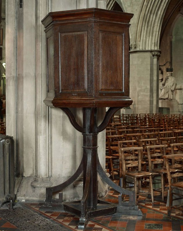 Деревянная церковная кафедра внутри собора: высокий ящик-кафедра на стойке, вокруг — ряды деревянных скамей и алтарные арки.