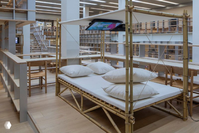 Интерьер с дизайнерским мебельным объектом в виде кровати среди стеллажей — декоративная деталь и место для отдыха внутри библиотеки.