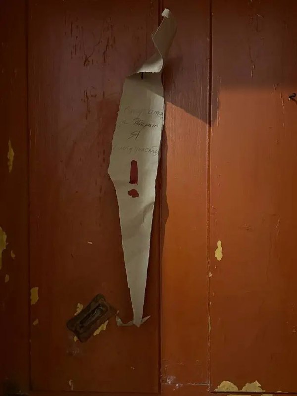 Дверь с облупившейся краской и оторванным слоем обоев — деталь аутентичной коммунальной квартиры, подчёркивающая следы времени и предыдущих ремонтов.