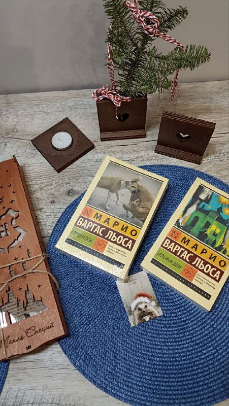 Деревянные сувениры и две книги Марио Варгаса Льосы на круглой синей подставке — домашняя композиция с книжными находками.