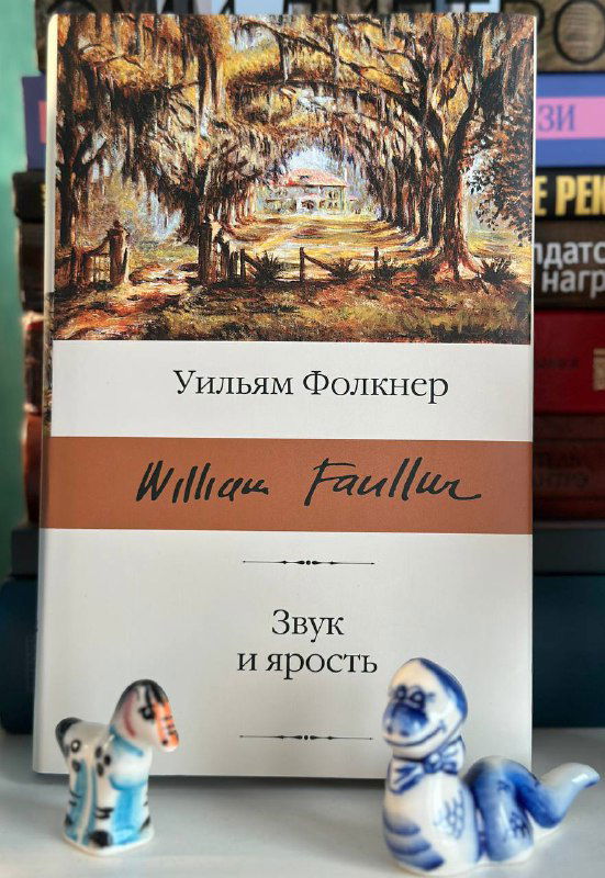 Тонкий том Уильяма Фолкнера «Звук и ярость» на полке; рядом небольшие фарфоровые фигурки, уютный книжный интерьер.