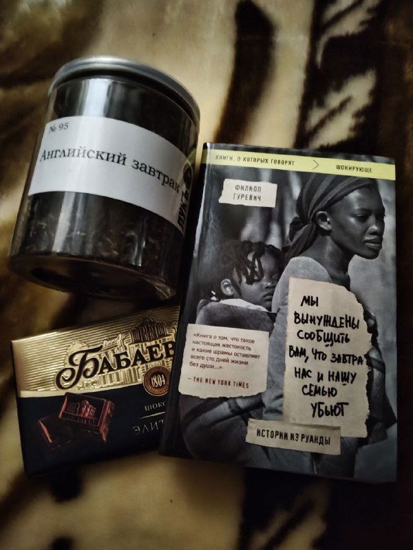 Фотография баночки и упаковок с напитками рядом с книгообложкой на столе; бытовой кадр с акцентом на мелочи и чтение с чашкой.