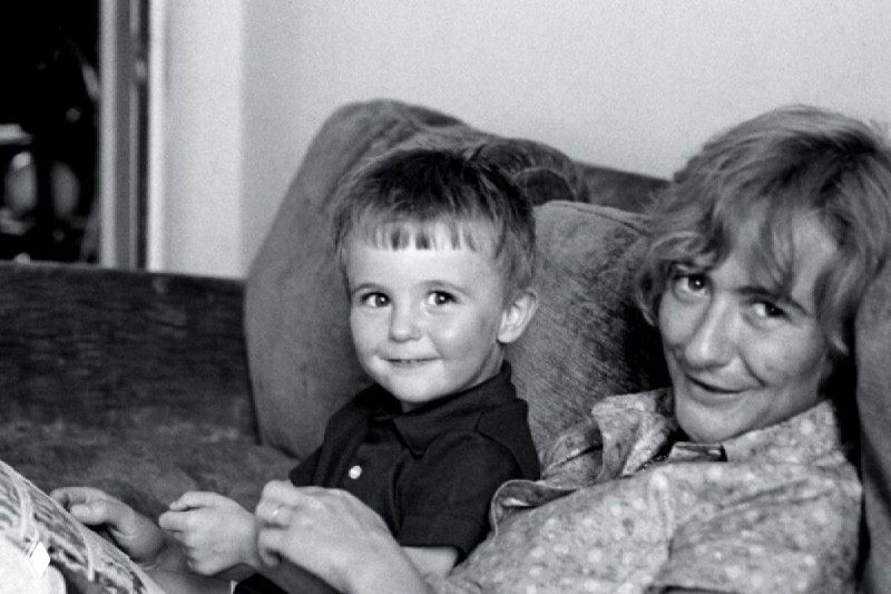 Чёрно‑белая архивная фотография: ребёнок и женщина на диване, домашний семейный кадр в книжном контексте, мягкий семейный портрет.