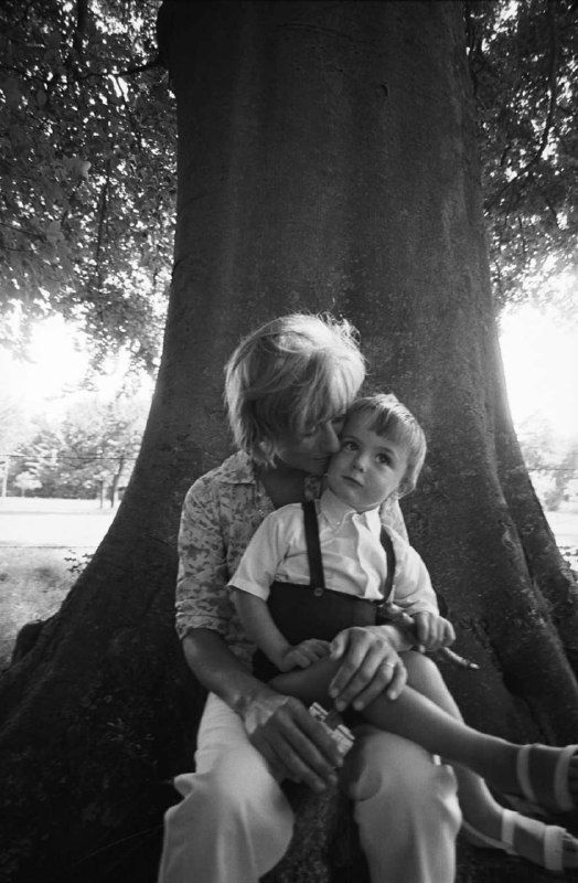Чёрно‑белая фотография женщины с ребёнком под большим деревом в парке — интимный семейный кадр, натуралистичная сцена на открытом воздухе.