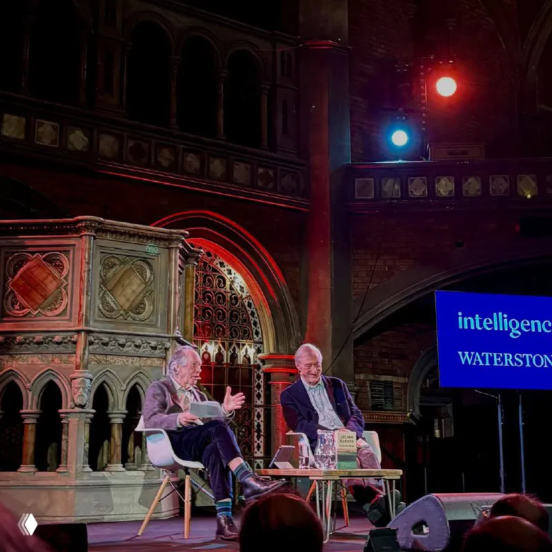 Беседа на сцене Union Chapel: Джулиан Барнс и Иэн Макьюэн сидят в креслах, стопка книг и микрофоны на фоне архитектуры зала.