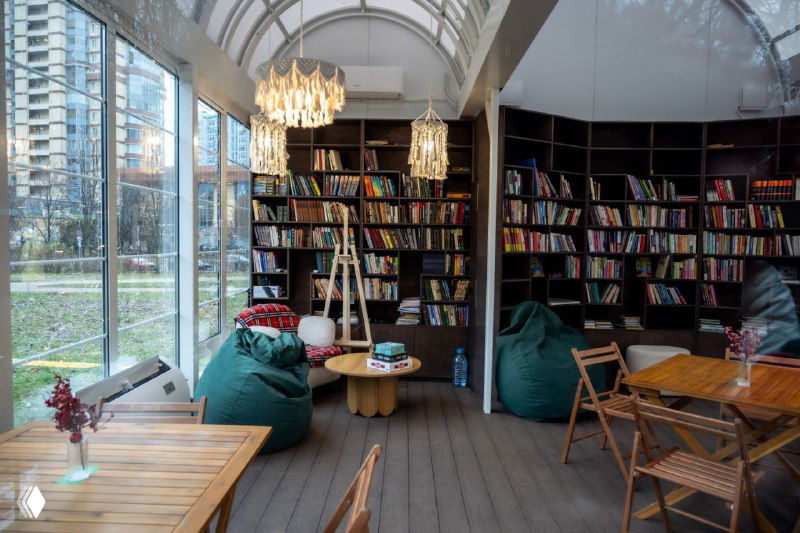 Интерьер павильона: полки с книгами вдоль стен, кресла-мешки и деревянные столы — тёплая уютная читальная зона в парке.