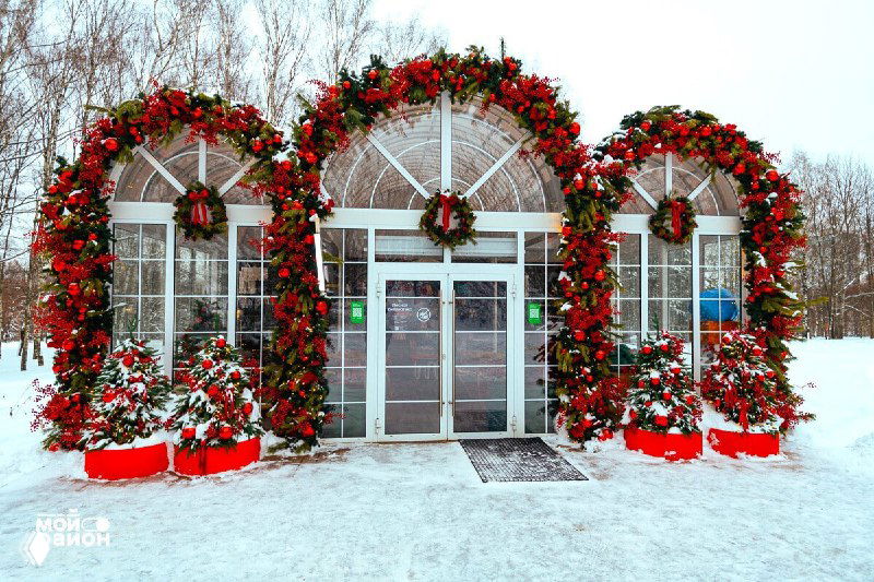 Вход в зимний павильон библиотеки, украшенный рождественскими венками и красными декорациями на фоне заснеженного парка.