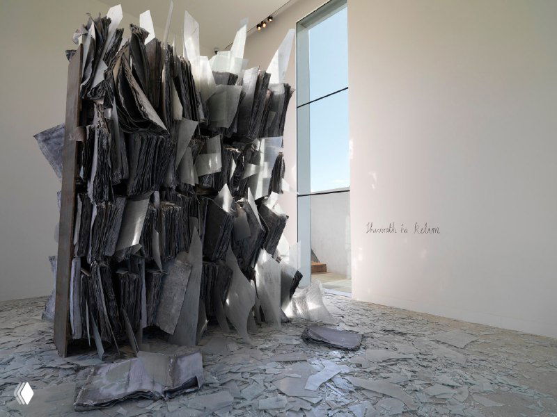 Объёмная инсталляция из свинцовых или тяжёлых листов в галерейном пространстве, разбросанные фрагменты и следы разрушения на полу.