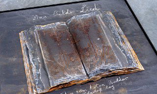 Крупный план книги-объекта: потёртые страницы, тёмные и ржавые следы, книга как символ тяжёлой и токсичной исторической памяти.