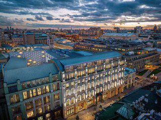 Ночной панорамный вид на отреставрированный дом на Кузнецком мосту, освещённый фасад комплекса Kuznetsky Most 12 и крыши центральной части города.