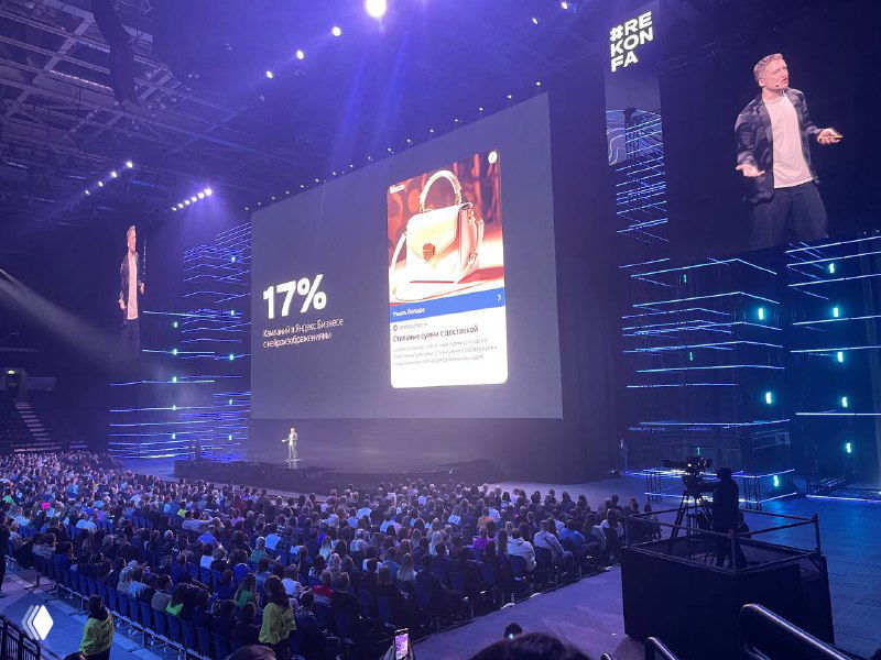 Экран конференции с процентной статистикой 17% и примером рекламного объявления; сцена освещена, зрители внизу кадра слушают спикера.