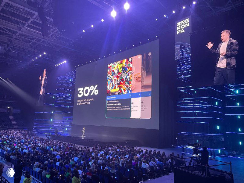 Презентация на сцене Rekonfa с данными 30% и примером креатива на большом экране; докладчик справа, аудитория внизу кадра.
