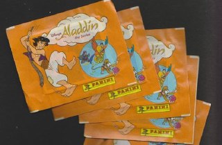 Стопка запечатанных оранжевых пакетиков с наклейками Panini «Aladdin», на тёмном фоне видны фирменные рисунки и логотип издателя на упаковках.