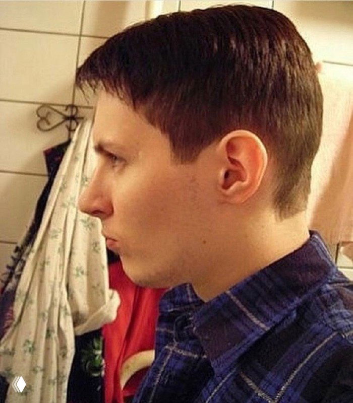 Профильный портрет в ретро-стиле: молодой человек в клетчатой рубашке на фоне плитки и занавески, плотный кадр в ванной.