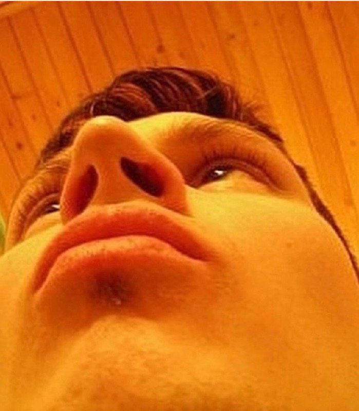 Низкий ракурс крупным планом: подбородок и ноздри в фокусе, тёплый оттенок освещения и деревянный фон под углом.