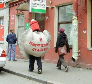 Человек в ростовом костюме пельменя на городской улице с надписью на спине — комичная и немного унизительная уличная сцена.