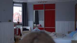 Кадр-превью из видео: интерьер комнаты с кроватью, тумбой, зеркальным шкафом красного цвета и окном на дальнем плане.