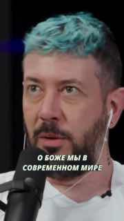 Крупный план мужчины в наушниках и с подсвеченными голубыми волосами в подкастовой/студийной обстановке; кадр с наложенной текстовой фразой о современном мире.