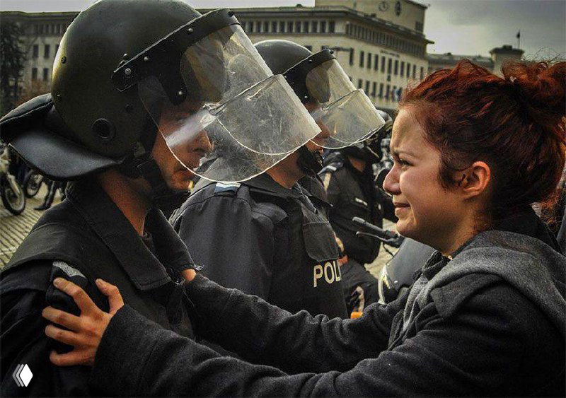 Разговор по душам: молодая плачущая женщина прижимает руки к груди полицейскому в экипировке — личная драма на фоне линейной охраны порядка.