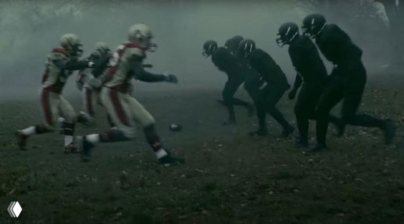 Сцена массового противостояния на поле: игроки в красной форме сталкиваются с игроками в черной форме, туман и драматичное освещение создают ощущение конфликта.