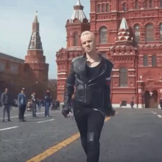 Кадр из клипа: белокурый исполнитель в чёрной кожаной куртке идёт по Красной площади на фоне исторических зданий Москвы, эпичный городской контекст.