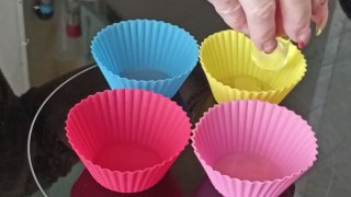 Фотография четырёх цветных силиконовых формочек на стеклокерамической плите; видна рука, подготавливающая посуду для яйца пашот.