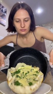 Вертикальное видео: автор держит сковороду с готовой яичницей в лаваше — творог, шпинат и сыр видны сверху, кухонный фон.