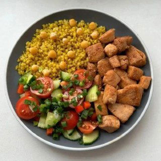 Тарелка с булгуром или смесью круп, кус-кусом и обжаренными кубиками мяса рядом с овощным салатом — миска с цветными ингредиентами, вид сверху.