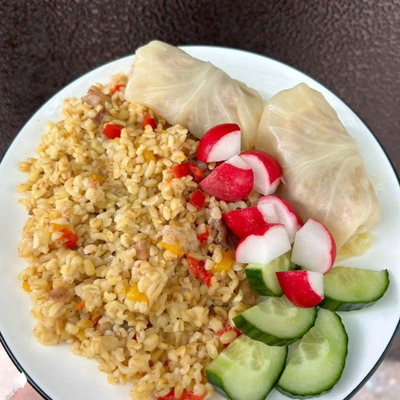 Тарелка с булгуром или рисом, двумя голубцами и ломтиками редиски и огурца — домашний ПП-обед, аккуратно сервирован на белой тарелке.