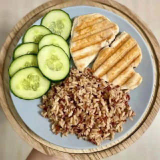 Тарелка с миксом из бурого риса или булгура, двумя кусочками грудки на гриле и ломтиками огурца — лёгкий ПП-обед, аккуратно выложен на тарелке.