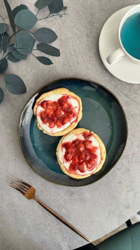 Две творожные ватрушки с крошками свежей клубники сверху на тёмной тарелке, рядом столовая вилка — десертный вариант без сахара.