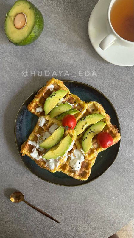 Порция тыквенных вафель на тёмной тарелке с ломтиками авокадо, помидором и творожным сыром — питательная подача.