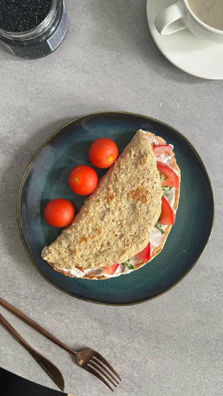 Сложенный тост или лепешка с помидорами, зеленью и сыром на тарелке; минималистичная сервировка и чашка напитка рядом.