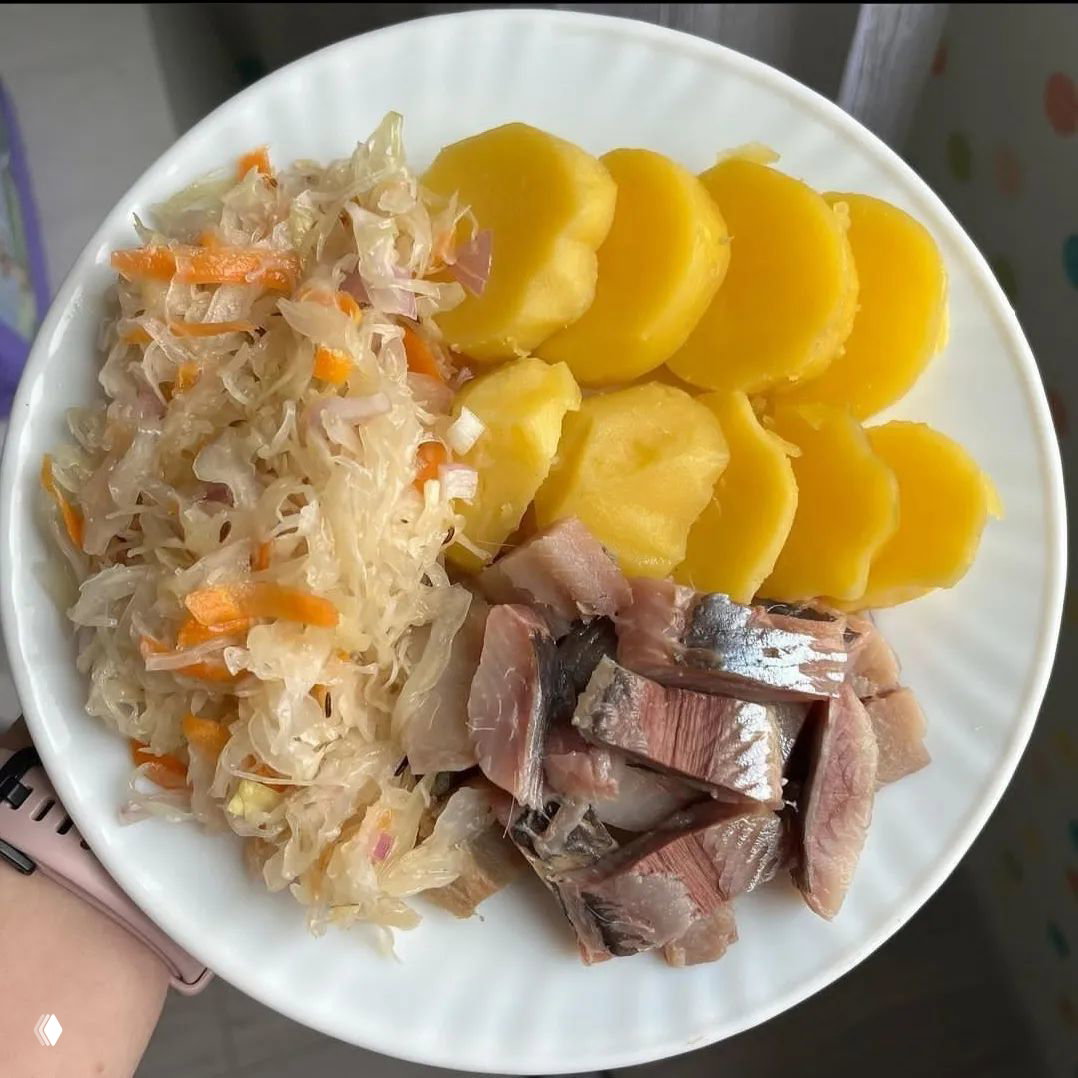 Тарелка с отварным картофелем, квашеной капустой и кусочками сельди — традиционный вариант обеда с рыбой и гарниром.