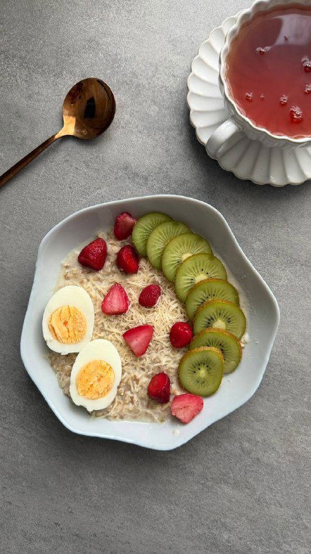 Тарелка с овсяной кашей на молоководе, добавленным белком, дольками киви и ягодами, варёное яйцо и творожный сырок на фоне столовой посуды.