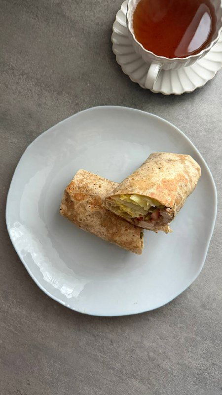 Разрезанная тортилья с видимой начинкой из индейки и овощей на белой тарелке — удобный завтрак в дорогу или на работу.